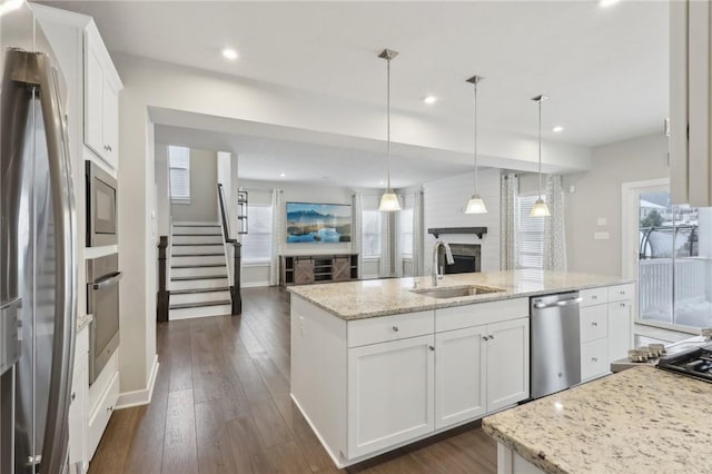 kitchen featuring white cabinetry, sink, hanging light fixtures, stainless steel appliances, and an island with sink