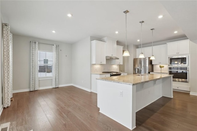 kitchen featuring tasteful backsplash, stainless steel appliances, a kitchen island with sink, white cabinets, and hanging light fixtures