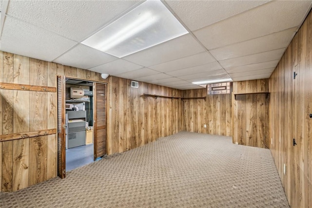 basement with carpet flooring, a drop ceiling, and wood walls