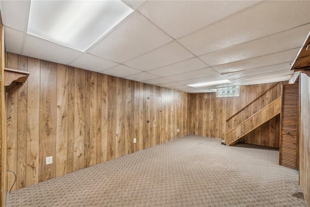 basement featuring carpet, a drop ceiling, and wood walls