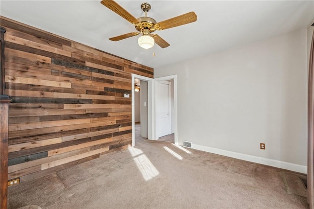 spare room featuring carpet, ceiling fan, and wood walls