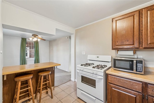 kitchen with ceiling fan, white gas stove, a breakfast bar, light tile patterned floors, and ornamental molding