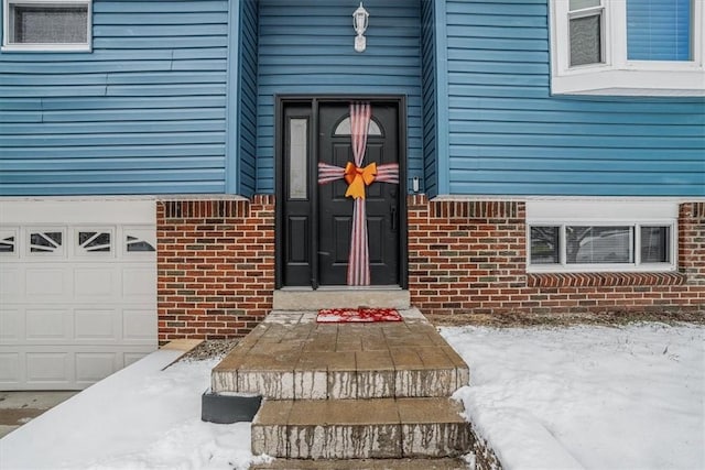 snow covered property entrance with a garage and a wall unit AC