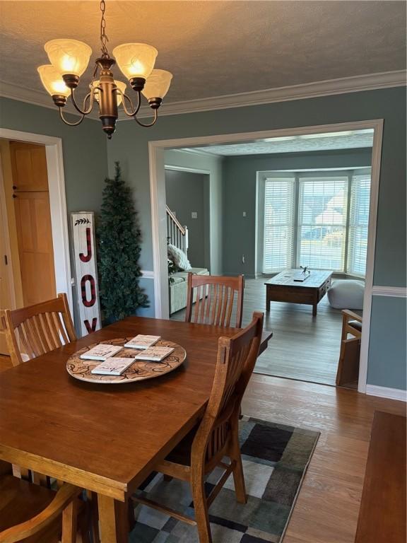 dining area with hardwood / wood-style floors, a notable chandelier, crown molding, and a textured ceiling