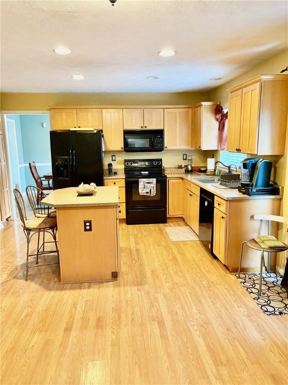 kitchen featuring black appliances, sink, light wood-type flooring, light brown cabinetry, and a kitchen island