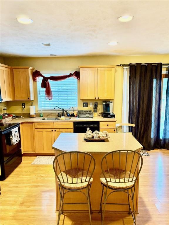 kitchen with black appliances, light brown cabinets, a kitchen island, and sink