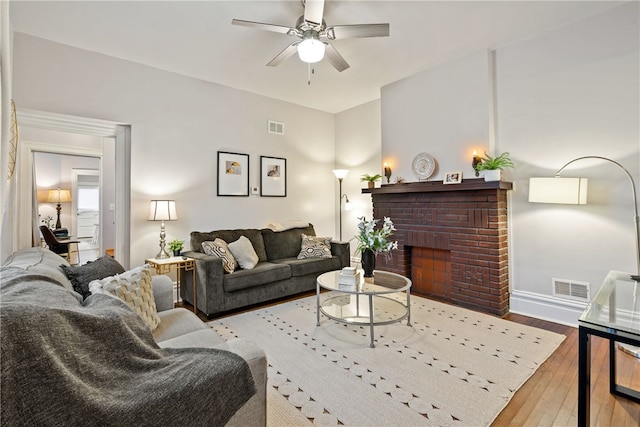 living room with light wood-type flooring, a brick fireplace, and ceiling fan