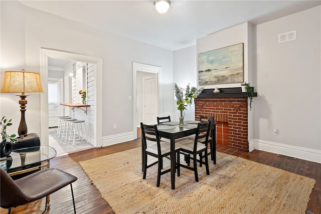 dining space featuring dark hardwood / wood-style flooring and a brick fireplace