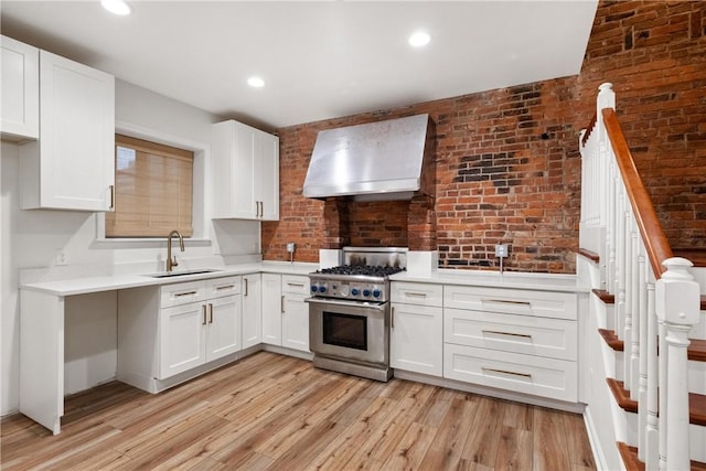 kitchen with white cabinets, stainless steel stove, wall chimney exhaust hood, and sink