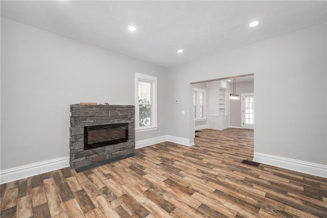 unfurnished living room with wood-type flooring, a stone fireplace, and a wealth of natural light