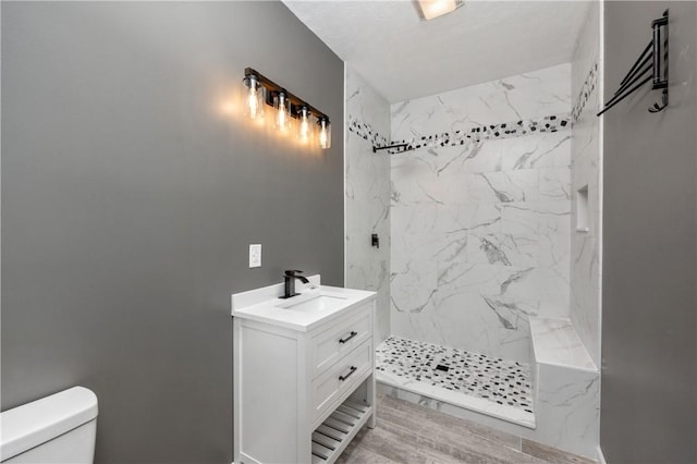 bathroom with a tile shower, vanity, wood-type flooring, and toilet