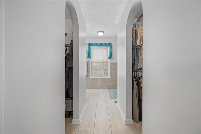 hallway with ornamental molding, a textured ceiling, and tile walls