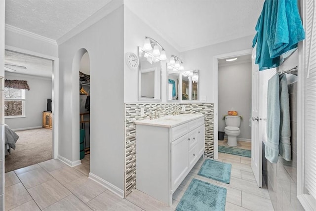 bathroom featuring vanity, backsplash, toilet, ornamental molding, and a textured ceiling