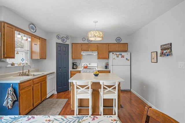 kitchen with pendant lighting, a center island, white appliances, sink, and hardwood / wood-style flooring