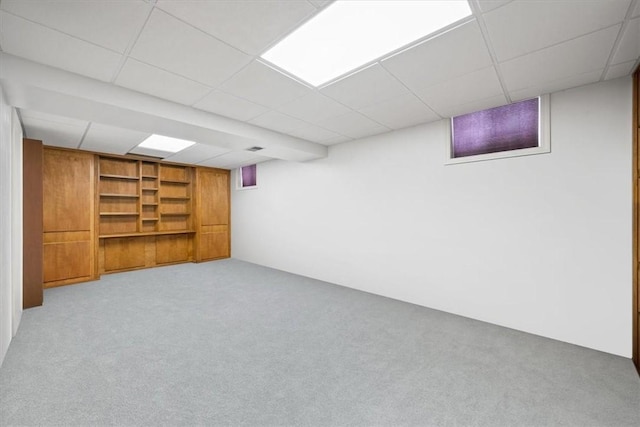 basement with a paneled ceiling, light carpet, and built in features