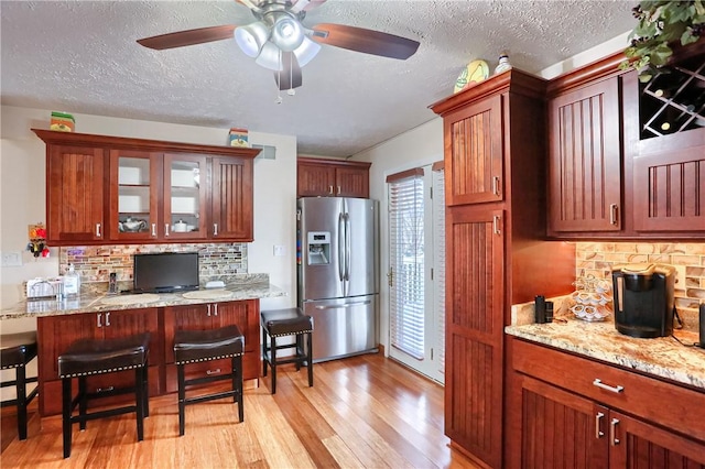 kitchen with stainless steel refrigerator with ice dispenser, decorative backsplash, a breakfast bar, and light hardwood / wood-style flooring