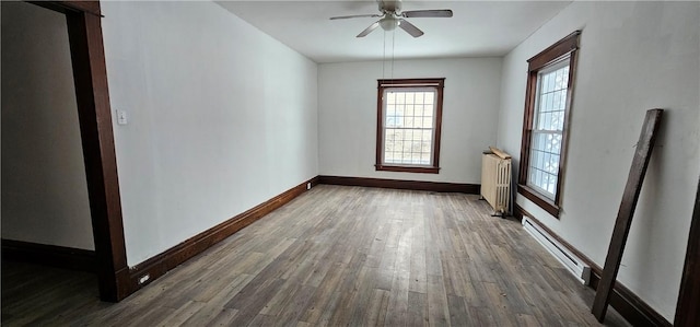 empty room featuring dark hardwood / wood-style floors, radiator, a baseboard heating unit, and ceiling fan