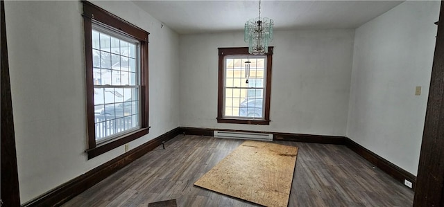 empty room with a notable chandelier, dark hardwood / wood-style flooring, and a baseboard heating unit