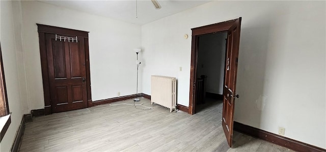 empty room featuring ceiling fan, light wood-type flooring, radiator, and a baseboard radiator