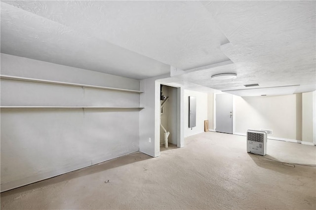 basement with a textured ceiling, heating unit, and light colored carpet