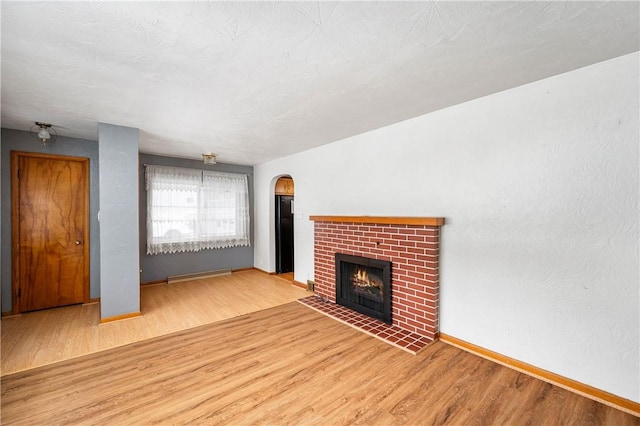 unfurnished living room featuring a brick fireplace, a baseboard heating unit, and light hardwood / wood-style flooring