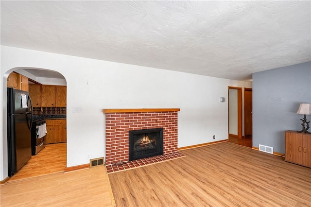 living room with light wood-type flooring, a brick fireplace, and a textured ceiling