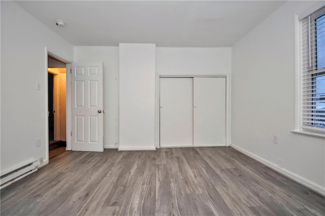 unfurnished bedroom featuring a closet, hardwood / wood-style floors, and a baseboard heating unit