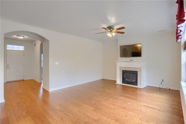 unfurnished living room with a tile fireplace, light wood-type flooring, and ceiling fan