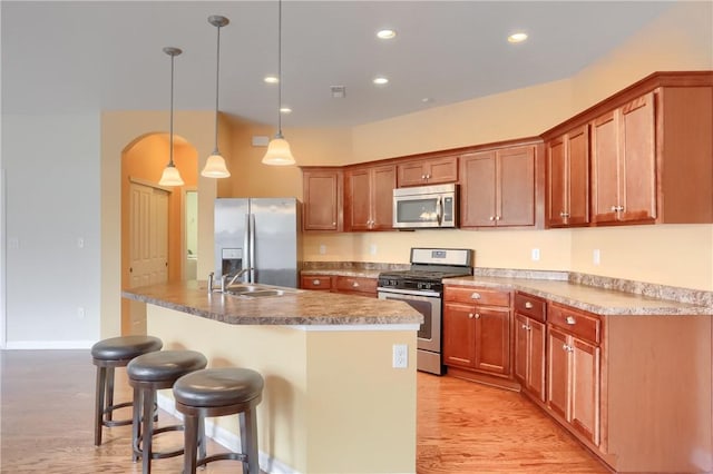 kitchen featuring a breakfast bar, sink, hanging light fixtures, light hardwood / wood-style flooring, and appliances with stainless steel finishes