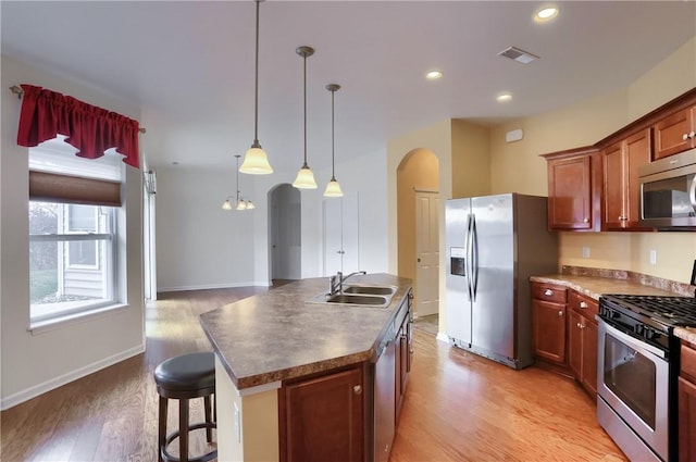 kitchen with sink, stainless steel appliances, pendant lighting, light hardwood / wood-style floors, and a kitchen island with sink