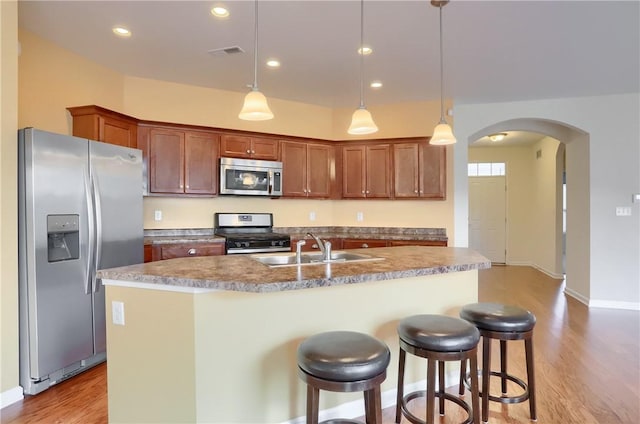 kitchen with a breakfast bar, stainless steel appliances, sink, pendant lighting, and a center island with sink