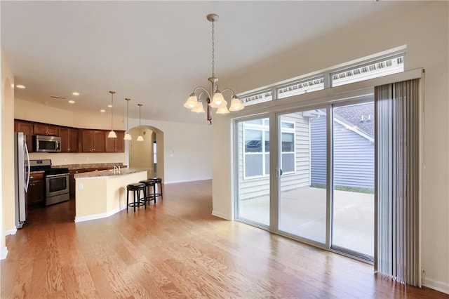 kitchen with hardwood / wood-style floors, decorative light fixtures, a notable chandelier, a kitchen bar, and stainless steel appliances