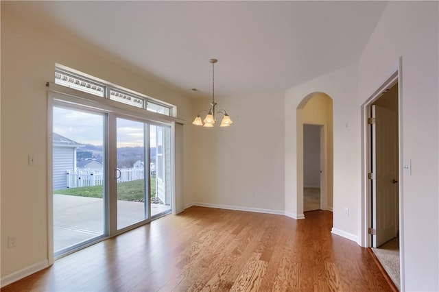 empty room with wood-type flooring and an inviting chandelier