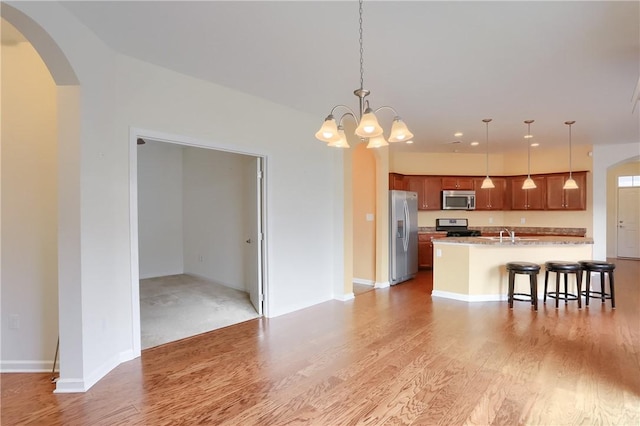 kitchen with a kitchen bar, stainless steel appliances, a kitchen island with sink, a chandelier, and hanging light fixtures