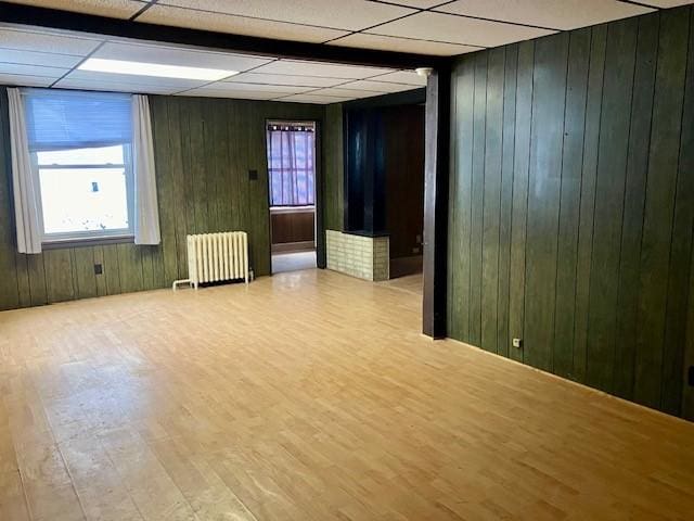 empty room with wooden walls, a drop ceiling, light wood-type flooring, and radiator