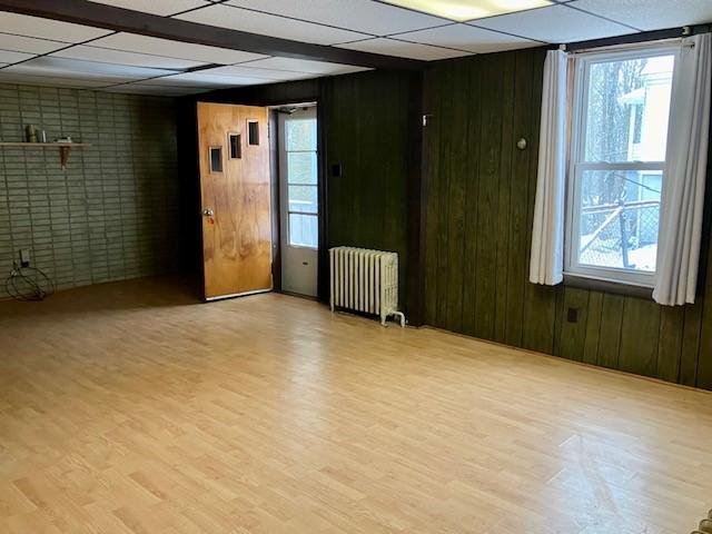 empty room with radiator, wooden walls, and light wood-type flooring