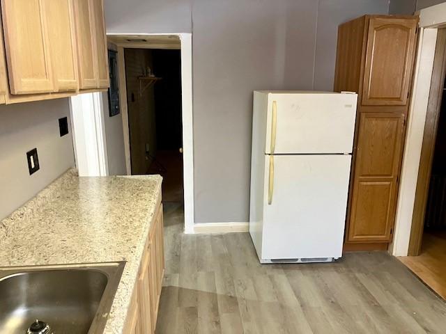 kitchen with light stone countertops, light brown cabinetry, light hardwood / wood-style floors, sink, and white fridge