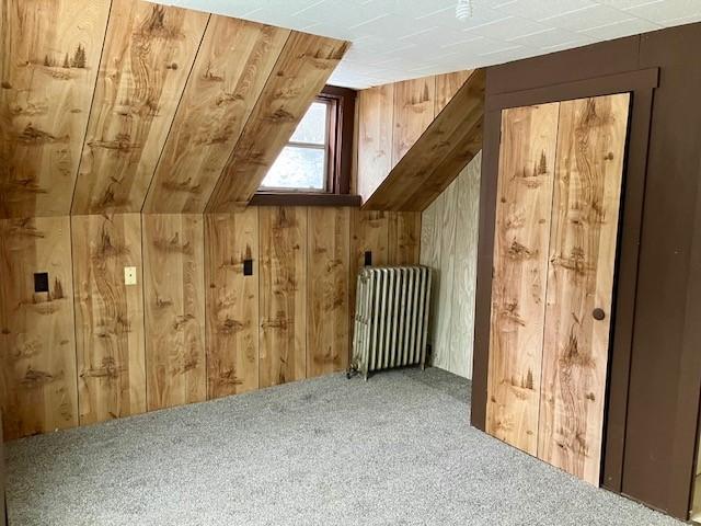 bonus room featuring wood walls, radiator heating unit, carpet, and lofted ceiling