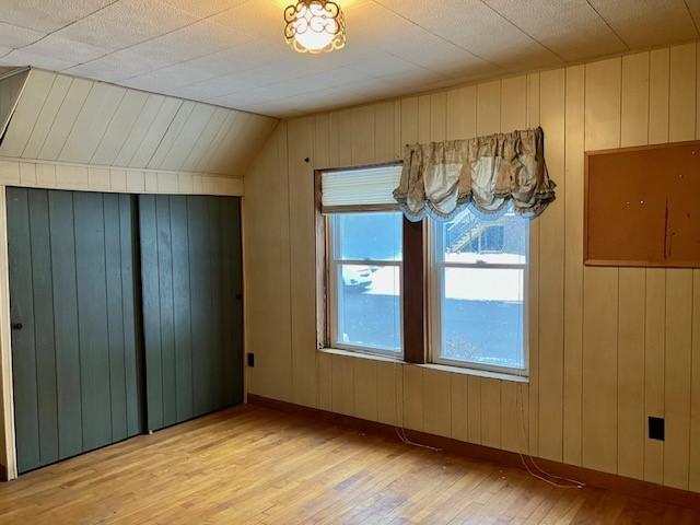 bonus room featuring wood walls, light hardwood / wood-style floors, and vaulted ceiling