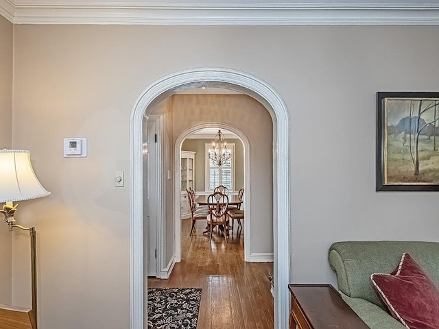 corridor featuring crown molding, wood-type flooring, and an inviting chandelier