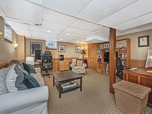 carpeted living room featuring wooden walls and a drop ceiling