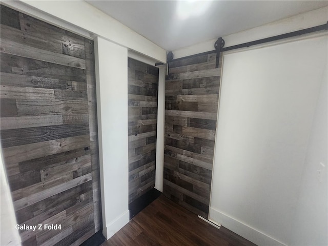 corridor with wood walls, a barn door, and dark wood-type flooring