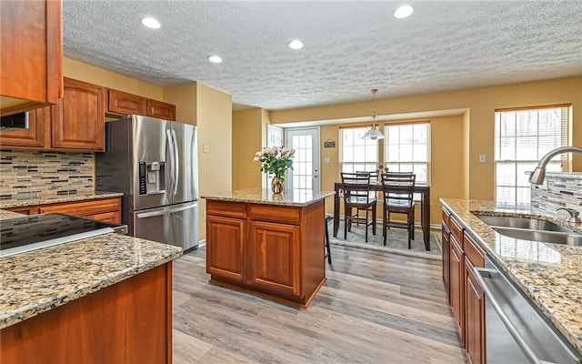 kitchen featuring appliances with stainless steel finishes, decorative light fixtures, tasteful backsplash, sink, and light wood-type flooring