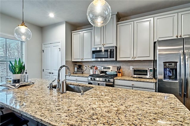 kitchen with pendant lighting, sink, decorative backsplash, appliances with stainless steel finishes, and light stone counters