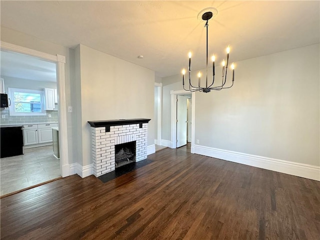 unfurnished living room with dark hardwood / wood-style floors, a brick fireplace, and a notable chandelier