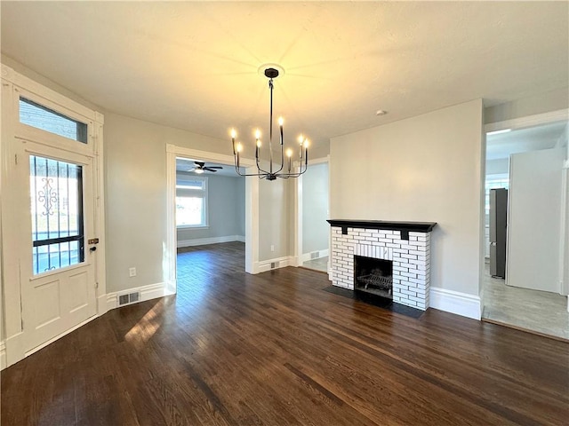 unfurnished living room with ceiling fan with notable chandelier, dark hardwood / wood-style floors, and a brick fireplace