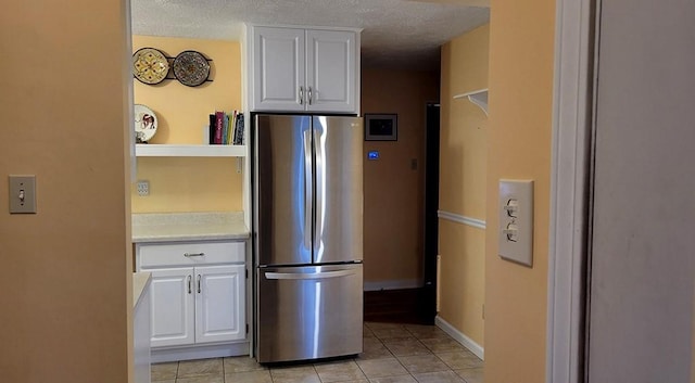 kitchen with stainless steel fridge, white cabinetry, a textured ceiling, and light tile patterned floors