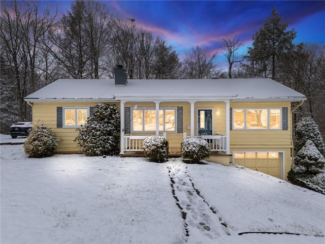 snow covered rear of property featuring a porch and a garage