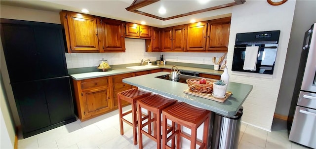 kitchen featuring a breakfast bar, a kitchen island with sink, sink, stovetop, and oven