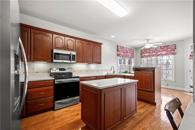 kitchen featuring sink, ceiling fan, light hardwood / wood-style floors, appliances with stainless steel finishes, and a kitchen island